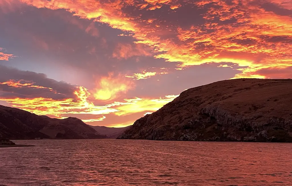 A fiery orange-and-pink sunset over a harbour ringed by dark hills